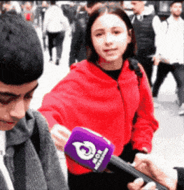 a girl in a red jacket is being interviewed by a man with a purple microphone that says ' vox '