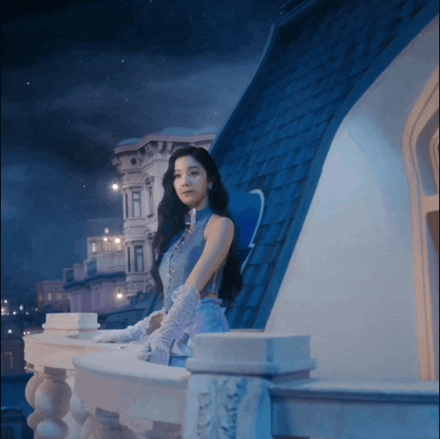 a woman in a blue dress and white gloves stands on a balcony overlooking a city