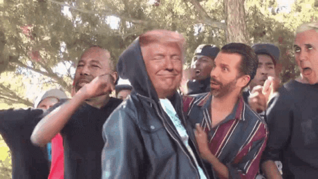 a group of men are standing around a man in a hoodie with a trump face on his face