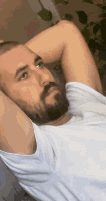 a man with a beard and a white shirt is laying on a couch with his hands behind his head
