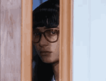 a woman wearing glasses is peeking through a doorway .