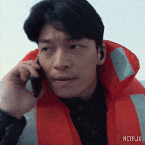 a man wearing an orange life jacket is talking on a cell phone with a netflix logo in the background