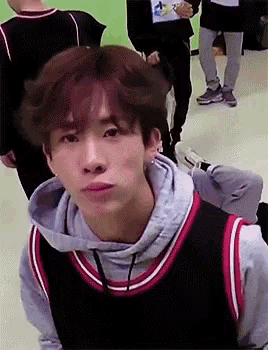 a young man wearing a basketball jersey and a hoodie is making a face .