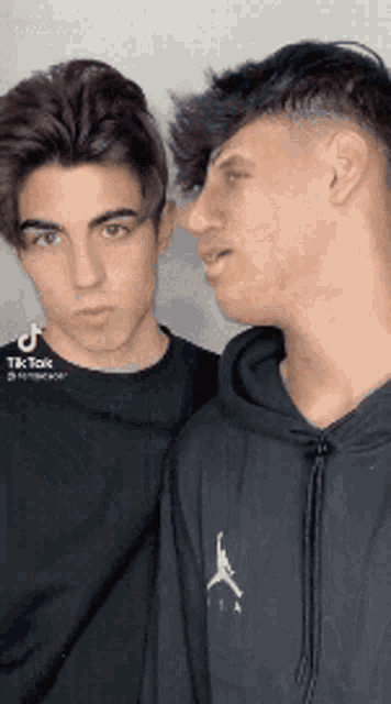 two young men are standing next to each other and one of them is wearing a hoodie .