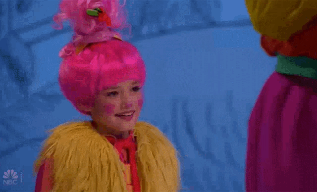 a little girl wearing a pink wig and a yellow fur coat .