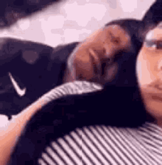 a man and a woman are laying on a bed . the woman is wearing a striped shirt .