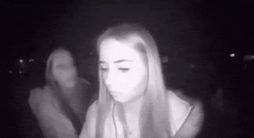 a woman is sitting in a dark room with a ghost in the background .