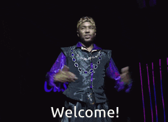 a man wearing a purple shirt and a crown is standing on a stage with his arms outstretched and says welcome