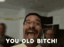 a man with a mustache and glasses is laughing and saying you old bitch .