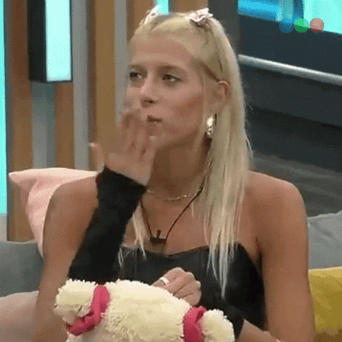 a blonde woman is holding a stuffed animal and covering her mouth