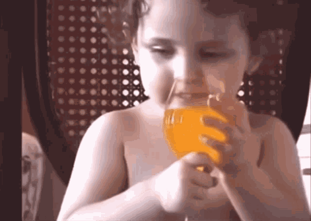 a young girl drinking orange juice from a glass