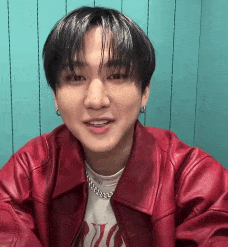 a close up of a young man wearing a red leather jacket and earrings .
