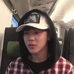 a man wearing a hat and a hoodie is sitting on a train .