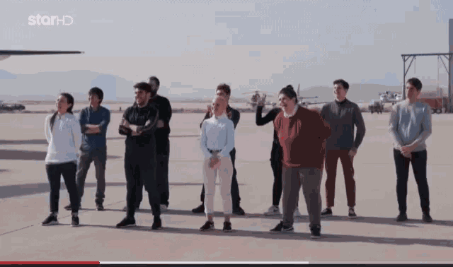 a group of people standing on a runway with starhd on the bottom right
