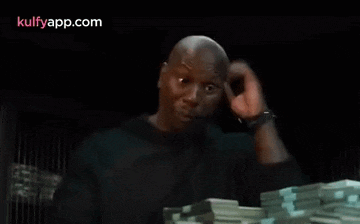 a man is standing in front of a pile of money and making a funny face .