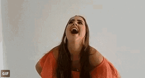 a woman in a red dress is laughing and waving her hand in front of a white wall .