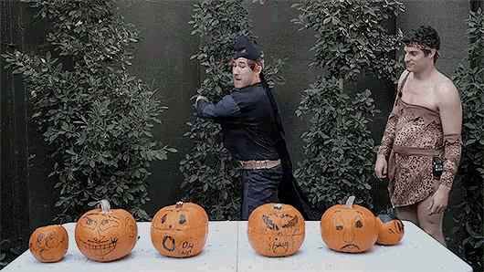 a man in a batman costume stands next to a table of pumpkins with faces carved into them