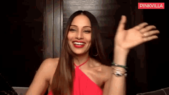 a woman in a red dress is smiling and waving her hand .