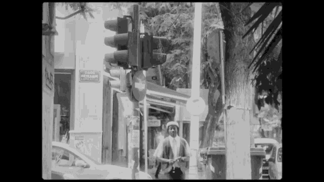 a black and white photo of a man standing in front of a traffic light with a sign that says gade aethanae
