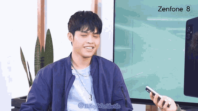 a man in a blue jacket is smiling in front of a zenfone 8 screen