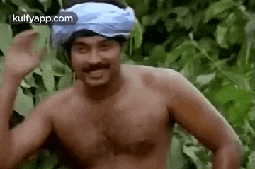 a shirtless man with a turban on his head is standing in the jungle .