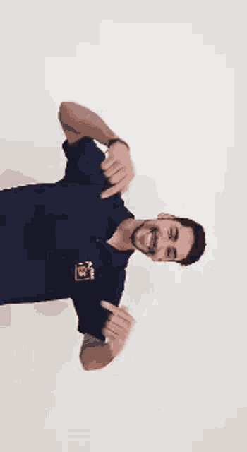 a man in a blue shirt is dancing with his arms outstretched against a white background .