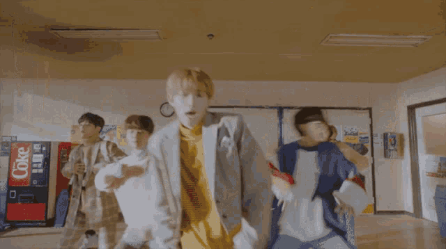 a group of people are dancing in a hallway with a coke vending machine in the background