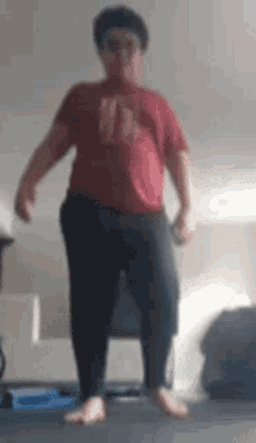 a man in a red shirt and black pants is standing on one leg in a room .
