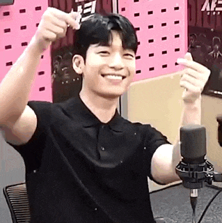 a young man in a black shirt is sitting in front of a microphone and making a heart shape with his hands .