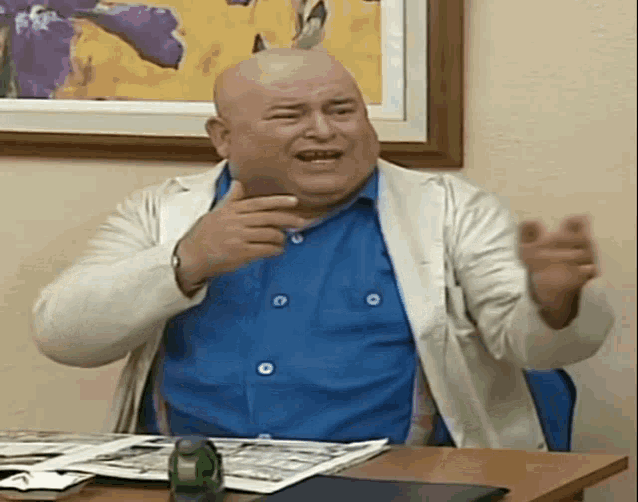 a bald man is sitting at a desk in front of a painting .