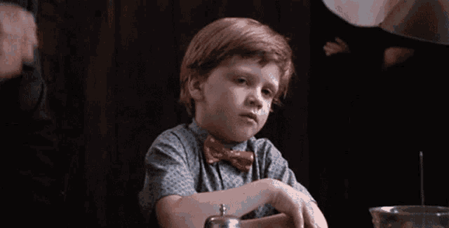 a young boy is sitting at a table covering his nose with his hand