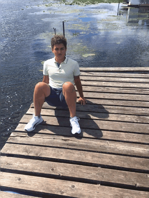 a young man sits on a wooden dock near a lake