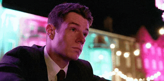 a man in a suit and tie sits in front of a pink building