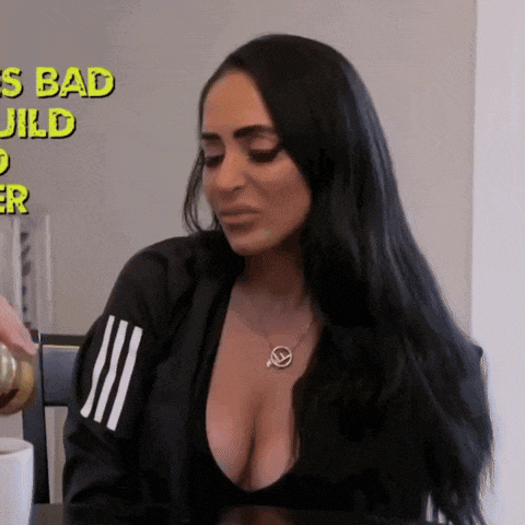 a woman with long black hair is sitting at a table with her breasts exposed .