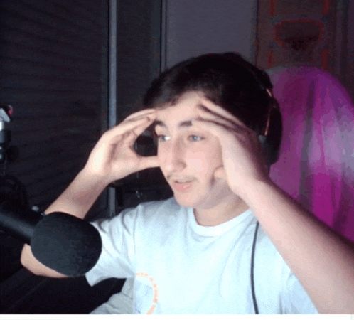 a young man wearing headphones and a white shirt holds his hands to his head