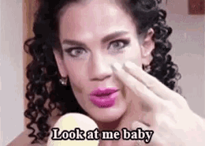 a woman with curly hair is holding a sponge to her face and saying `` look at me baby '' .