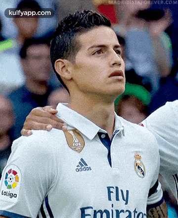 a soccer player wearing a fly emirates shirt stands in front of a crowd .