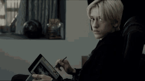 a young man sits in a chair using a tablet computer