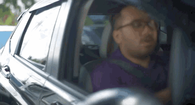 a man is sitting in the driver 's seat of a car looking out the window .