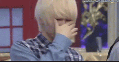a man with blonde hair is covering his face with his hands .