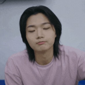 a man with long hair is wearing a pink shirt and making a funny face .