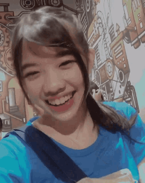 a girl in a blue shirt is smiling in front of a wall with gears