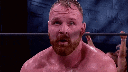 a wrestler with a beard is standing in a wrestling ring with his mouth open .