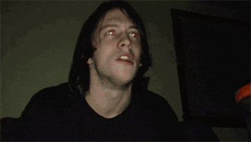 a man with red eyes is looking up at the camera in a dark room .