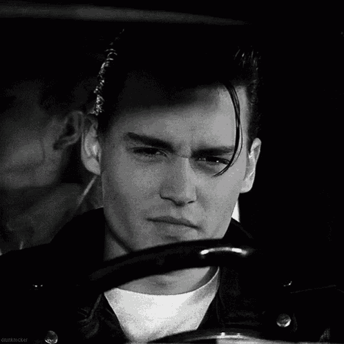 a man in a leather jacket is smiling in a black and white photo while driving a car .