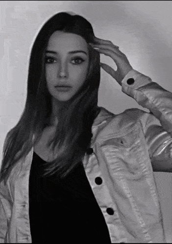 a black and white photo of a woman in a white jacket touching her hair