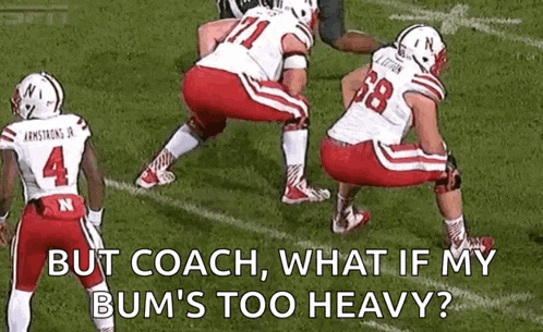 a group of football players are squatting on a field and talking to each other .