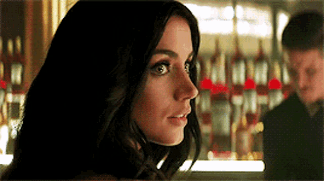 a woman is standing in front of a bar with bottles of alcohol in the background .