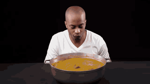 a man in a white shirt is smelling a large pot of soup