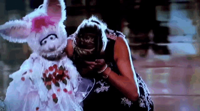 a woman is kneeling down next to a stuffed rabbit with flowers on it 's face .